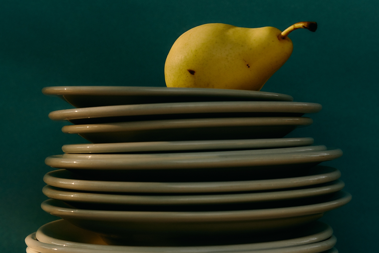 A stack of dirty plates with a ripe yellow pear balanced on top, symbolizing imbalance or a messy workload.