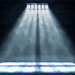 beam of light shines through high barred windows into a dark, empty cell, casting long shadows on the concrete floor—evoking the isolation and quiet heaviness of both prisons and hospital rooms.